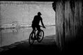 Sillhouette of a Male Cyclist Riding Underneath a Canal Under a Bridge.