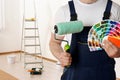 Male decorator with paint roller and color palette samples in empty room. Space for text Royalty Free Stock Photo