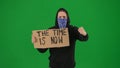 A male demonstrator with his face covered by a scarf holds up a sign that says Time is now. The man on a green screen