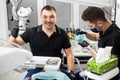 Male dentist with ceramic braces is smiling to the camera while another is working with medical instruments