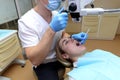 Dentist examines a young beautiful woman, looks at her teeth with a professional microscope in a surgical dental office