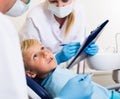 Male dentist with girl assistant are diagnosticating to young patient which is sitting