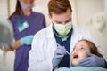 Male dentist looking with dental mirror child`s teeth