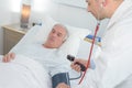 male doctor checking senior mans blood pressure in hospital