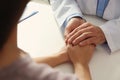 Male doctor comforting woman at table, closeup of hands.