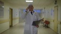 Male doctor dressed in lab coat is walking through the corridor of the ward and examinating roentgenogram of a patient