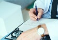 Male doctor on duty in white coat with pen in hand filling prescription or checklist document close up. Selective focus Royalty Free Stock Photo