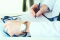 Male doctor on duty in white coat with pen in hand filling prescription or checklist document close up. Selective focus Royalty Free Stock Photo