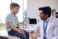 Male Doctor Or GP Wearing White Coat Examining Smiling Boy Testing Reflexes Royalty Free Stock Photo