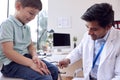 Male Doctor Or GP Wearing White Coat Examining Smiling Boy Testing Reflexes Royalty Free Stock Photo