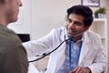 Male Doctor Or GP Wearing White Coat Examining Young Man Listening To Chest With Stethoscope Royalty Free Stock Photo