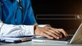 Male doctor hands typing on laptop computer keyboard,searching medical information with textbook on the desk at office.