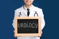 Male doctor holding small blackboard with word UROLOGY on blue background