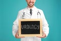 Male doctor holding small blackboard with word UROLOGY on turquoise background