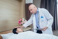 Male doctor holding tablet and touches forehead of female patient lying on bed to examine symptoms. Doctor takes care of patient Royalty Free Stock Photo