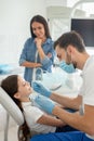 Male doctor with instruments in the hands looking girls teeth sitting in the dental chair while mother standing near her for Royalty Free Stock Photo