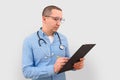 Male doctor making notes on a clipboard on a gray studio background. Royalty Free Stock Photo