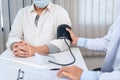 Male doctor in medical face mask is using sphygmomanometer to checking blood pressure to male patient Royalty Free Stock Photo