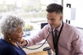 Male Doctor In Office Listening To Senior Female Patients Chest Using Stethoscope