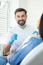 Male doctor smiling at the camera with instruments in the hands with client sitting in the dental chair