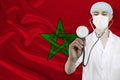 Male doctor with a stethoscope on the background of the silk national flag of Morocco, the concept of national medical care,