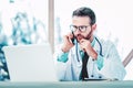 Male doctor talking on his mobile phone and using laptop while working in the doctor`s office Royalty Free Stock Photo