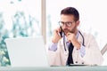 Male doctor using laptop and mobile phone while working in doctor`s room Royalty Free Stock Photo