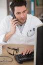 male doctor using mobile phone in clinic against computer Royalty Free Stock Photo