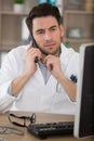 male doctor using telephone while working on computer in clinic Royalty Free Stock Photo