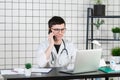 Male doctor using telephone while working on computer at table in clinic