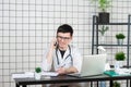 Male doctor using telephone while working on computer at table in clinic Royalty Free Stock Photo