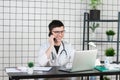 Male doctor using telephone while working on computer at table in clinic Royalty Free Stock Photo