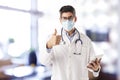 Male doctor wearing face mask and giving thumbs up while standing in the hospital