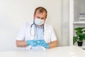 A male doctor, wearing a protective mask with a stethoscope, opens a package with a disposable syringe. close-up. Royalty Free Stock Photo