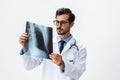 Male doctor in white coat and eyeglasses and stethoscope looking at patient X-rays for diagnosis on white Royalty Free Stock Photo