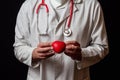 Male doctor in white coat and face mask and red stethoscope on his neck, Holding red heart in his hands, Health care theme Royalty Free Stock Photo