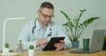 Male doctor in white coat using modern TabletPC device with touch screen. Doctor using DigitalTablet texting to patient