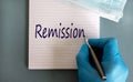 Male doctors hand in blue glove writes the word `remission` on a white note. Medicine mask. Beautiful blue background