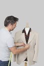 Male dressmaker adjusting suit on tailor's dummy over colored background