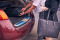 Male driver helping lady to put luggage in car trunk