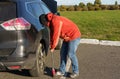 A male driver inflates a car wheel with a mechanical pump.