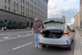 A male driver near a taxi car with an open trunk on a Moscow street.