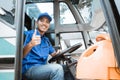 A male driver in uniform smiles at the camera with thumbs up while sitting behind the wheel Royalty Free Stock Photo