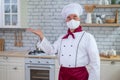 Male elderly chef in a medical mask in a restaurant kitchen Royalty Free Stock Photo