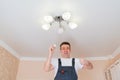 A male electrician changes the light bulbs in the ceiling light.