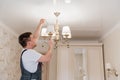 A male electrician changes the light bulbs in the ceiling light.