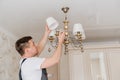 A male electrician changes the light bulbs in the ceiling light.