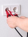 Male electrician measuring power on wall outlet with measuring device