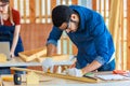 Male engineer architect foreman labor worker wears safety goggles using measuring tape measure wood plank on