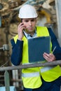 Male engineer in factory holding clipboard and talking on telephone